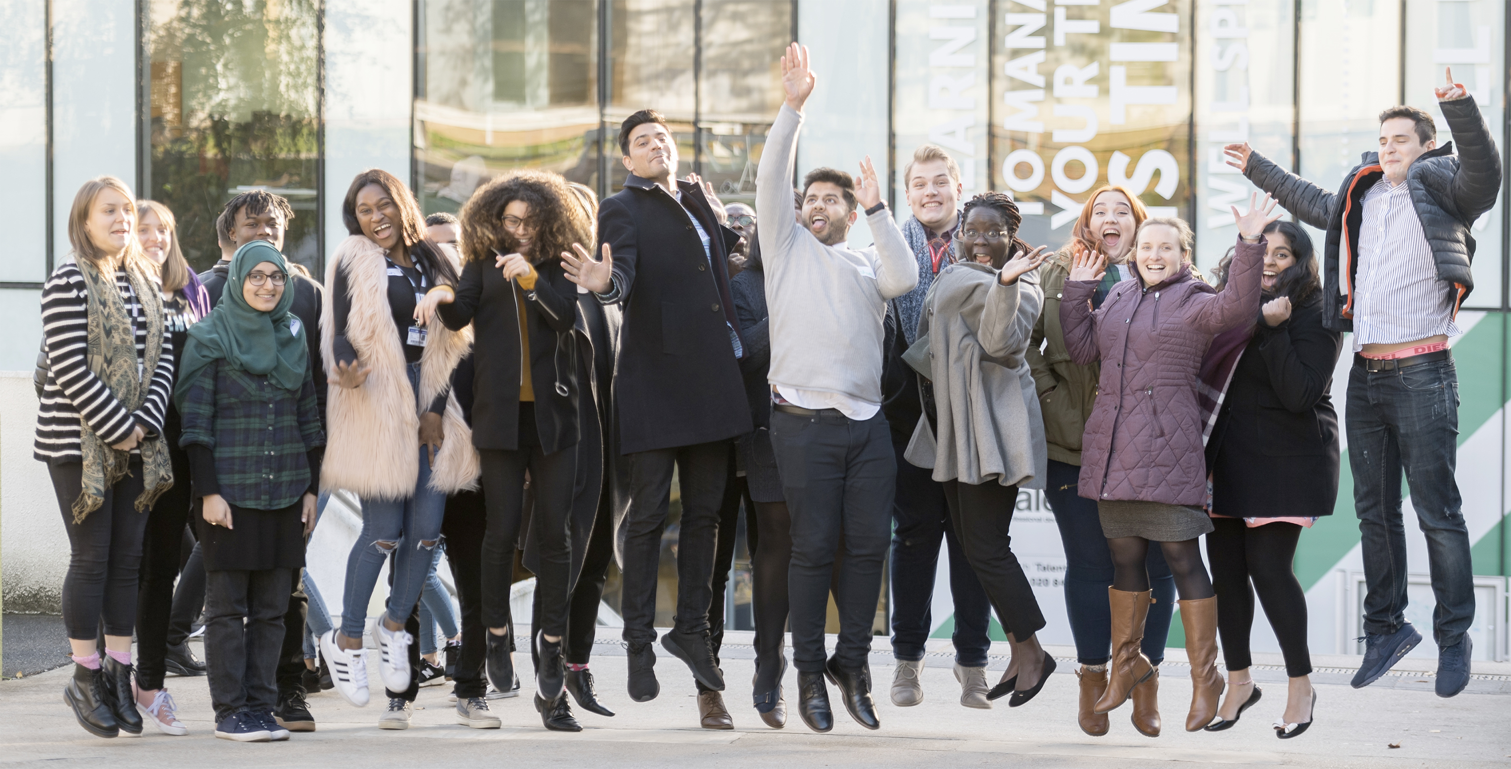 A group of students jumping up in front of a University building